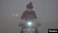 FILE - With a yellow smog alert in effect, a woman rides her electric bicycle along a street amid thick haze in Chiping county, Shandong province, China, Jan. 16, 2015.