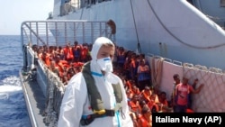 FILE - Migrants wait to be boarded on the San Giusto Navy ship, along the Mediterranean sea, off the Sicilian island of Lampedusa,, Aug. 23, 2014. 