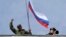 FILE - A man holds a Russian flag on the roof of the a navy building in Sevastopol, March 19, 2014.