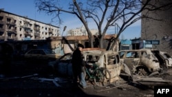 Un hombre con una bicicleta se encuentra cerca de coches quemados después de un ataque en Dobropillia, región de Donetsk, el 8 de marzo de 2025, en medio de la invasión rusa de Ucrania.