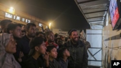 Palestinians watch a TV broadcast as they await the announcement of a ceasefire deal between Hamas and Israel, in Khan Younis, central Gaza Strip, Jan. 15, 2025.