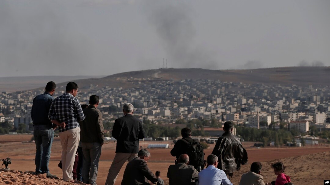 Warga mengamati asap membubung akibat pertempuran dengan ISIS dari Suruc, perbatasan Turki dan Suriah (15/10). (AP/Lefteris Pitarakis)