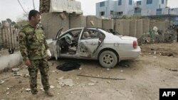 Polisi Irak berdiri di dekat sebuah mobil yang rusak dalam serangan bom bunuh diri di Baquba (foto: dok). Baquba diguncang serangan bunuh diri yang menewaskan 20 orang (6/4). 