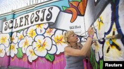FILE - Street artist Lydia Emily Archibald, who was diagnosed with multiple sclerosis in 2012, touches up her mural aimed at raising awareness about the disease in Los Angeles, April 9, 2015.