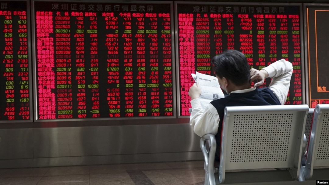 An investor reads a newspaper in front of electronic board showing stock information at a brokerage house in Beijing, China, Oct. 29, 2015. 