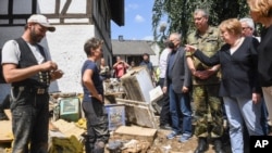 German Chancellor Angela Merkel, right, talks to residents during a visit to the flood-damaged village of Schuld near Bad Neuenahr-Ahrweiler, Germany, Sunday July 18, 2021. After days of extreme downpours causing devastating floods in Germany and…