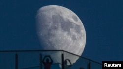 Visitors stand on the roof of a skyscraper as the moon rises over the skyline of Lujiazui financial district of Pudong in Shanghai, Aug. 16, 2013.