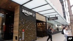 FILE - People walk out of an Amazon Go store in Seattle, Washington, March 4, 2020. Amazon is rolling out the Amazon One, a new device for contactless transactions that scans an individual’s palm. 