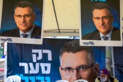 FILE - A Likud party member sits by a poster of veteran politician Gideon Saar from the governing Likud Party at a voting center in the northern Israeli city of Hadera, Dec. 26, 2019.