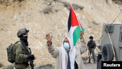 A demonstrator holding a Palestinian flag gestures as he stands next to Israeli forces during a protest against Israeli settlements in Masafer Yatta near Hebron, in the Israeli-occupied West Bank, Jan. 15, 2021. 