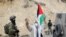 A demonstrator holding a Palestinian flag gestures as he stands next to Israeli forces during a protest against Israeli settlements in Masafer Yatta near Hebron, in the Israeli-occupied West Bank, Jan. 15, 2021. 