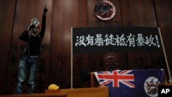 A protester shouts next to a defaced Hong Kong emblem and a banner reads "No thug, only tyranny" after they broke into the Legislative Council building in Hong Kong, Monday, July 1, 2019.