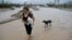 Una mujer carga a su perrito para protegerlo de la crecida de las aguas en Los Cabos, México.