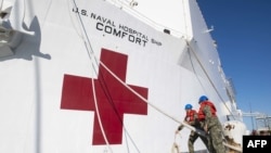 FILE - Boatswain's Mate 3rd Class Nathaniel Miller, left, and Logistics Specialist Seaman Apprentice Seth Stevens unmoor lines as the hospital ship USNS Comfort departs Norfolk, Va., June 14, 2019.