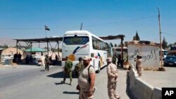 Pasukan pemerintah Suriah mengawasi evakuasi dengan bus pejuang Angkatan Darat Islam dari kota terkepung Douma, sebelah timur Damaskus, Suriah, Senin, 2 April 2018. (Foto: SANA via AP)