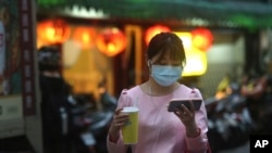 A woman in a protective face mask balances her cup while watching her smart phone in Taipei, Taiwan, on March 31, 2020.