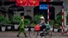 FILE - A woman rides a bicycle as a policeman walks past Vietnam flags in Hanoi, Vietnam, Feb. 27, 2019, 