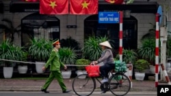 FILE - A woman rides a bicycle as a policeman walks past Vietnam flags in Hanoi, Vietnam, Feb. 27, 2019, 