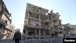 Wani mayakin 'yan tawaye akan hanyarshi a gaban wani gini da sojojin gwamnati suka fasa a unguwar Mleha dake birnin Damascus Junairu 21, 2013.