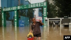 Seorang pria membawa air minum kemasan saat melintasi jalan yang banjir menyusul hujan lebat yang membanjiri dan menewaskan sedikitnya 33 orang pekan ini di kota Zhengzhou, provinsi Henan, China, 23 Juli 2021. (Foto: Noel Celis / AFP). 