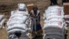 FILE - An Ethiopian woman stands by USAID sacks of wheat to be distributed by the Relief Society of Tigray in the town of Agula, in the Tigray region of northern Ethiopia, May 8, 2021. 