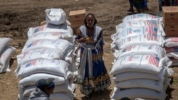 Seorang perempuan Ethiopia berdiri di dekat tumpukan karung gandum dari bantuan USAID yang disalurkan di Kota Agula, di utara Ethiopia, pada 8 Mei 2021. (Foto: AP/Ben Curtis)