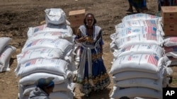 FILE - An Ethiopian woman stands by USAID sacks of wheat to be distributed by the Relief Society of Tigray in the town of Agula, in the Tigray region of northern Ethiopia, May 8, 2021. 