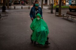 A man wearing a face mask and rain cover is pushed in a wheelchair along a boulevard in Barcelona, Spain, Sept. 9, 2020.