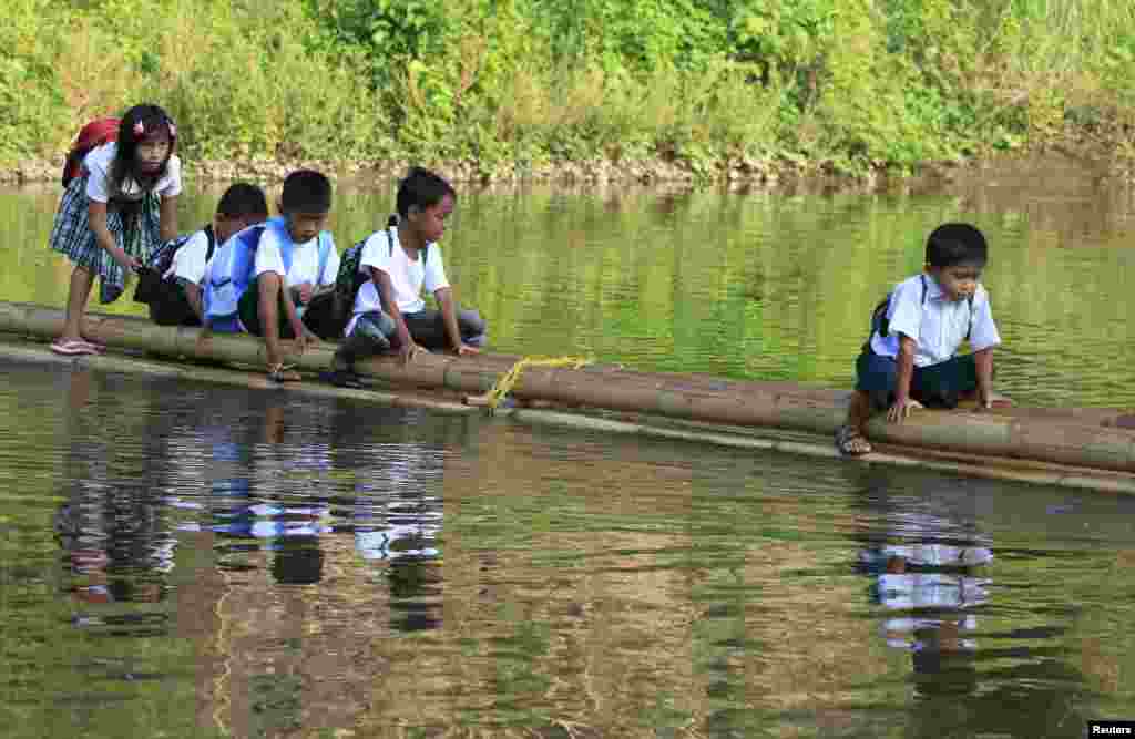 Students sit astride on a bamboo raft as they are ferried across a river on their way to Casili Elementary School for the first day of classes in Rodriguez, Rizal province, east of Manila, Philippines.