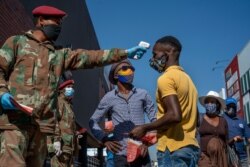 Un soldado toma la temperatura a un administrador de Taxis de Pan Africa, en el municipio de Alexandra, en Johannesburgo, el miércoles 20 de mayo de 2020. Sudáfrica tiene el mayor número de casos confirmados del nuevo coronavirus.