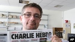 FILE - In this Sept.19, 2012 file photo, Stephane Charbonnier also known as Charb , the publishing director of the satyric weekly Charlie Hebdo, displays the front page of the newspaper as he poses for photographers in Paris.