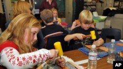 FILE - Idaho Arts Charter School students Maddison Thorpe, left, and Stefan Weiss work on their leather crafts as nationally known leather artist Deana Attebery shows the students the different kinds of tools of the trade in Nampa, Idaho, Dec. 9, 2008. The school received a National Endowment for the Arts grant to hold a series of folk arts after-school enrichment classes for at risk youths. 