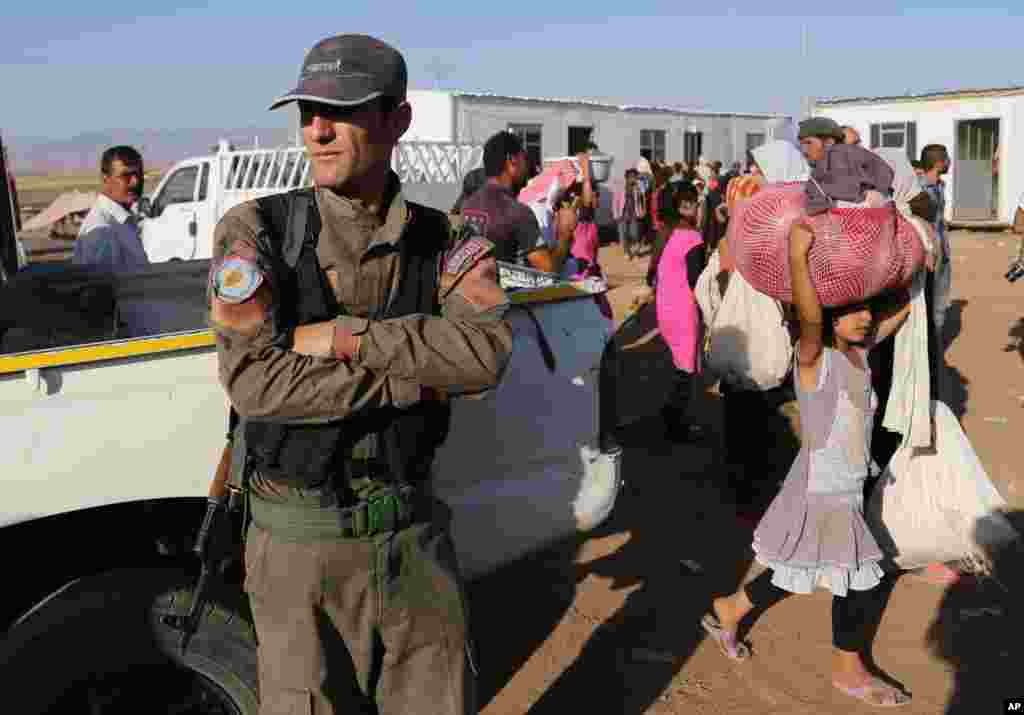 A Syrian Kurdish Peshmerga fighter stands guard as displaced Iraqis from the Yazidi community arrive at Nowruz camp, in Derike, Syria, Aug. 12, 2014. 