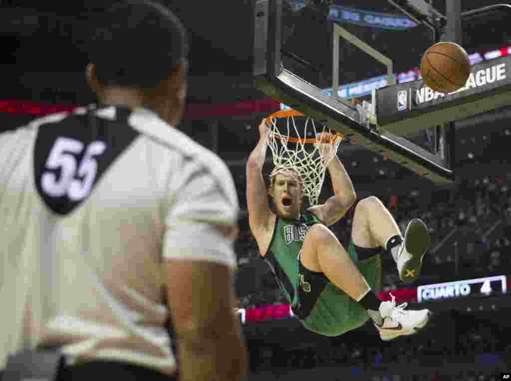 A referee watches as Boston Celtics Kelly Olynyk (41) swings from the basket after dunking during the second half of a regular-season NBA basketball game in Mexico City.