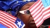 FILE - A market vendor stands among a group of women waving Liberian and American flags to show support for visiting U.S. Secretary of State Hillary Rodham Clinton, in Monrovia, Liberia. Obama recently lifted US sanctions on Liberia.