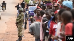 FILE - A Uganda People's Defence Forces (UPDF) soldier stands guard as supporters of Ugandan singer-turned-politician Robert Kyagulanyi, aka Bobi Wine, stand outside of Kyagulanyi's recording studios in Kampala's Kamwokya suburb, Aug. 27, 2018.