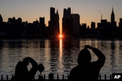 FILE - People view a Manhattanhenge sunrise along 42nd street in New York's Manhattan borough on Nov. 29, 2020, as viewed from Weehawken, N.J. There's still time to catch Manhattanhenge, when the setting sun aligns with the Manhattan street grid and bathes the urban canyons in a rosy glow. The last two Manhattanhenge sunsets of 2022 are Monday and Tuesday, July 11-12. (AP Photo/Yuki Iwamura, File)