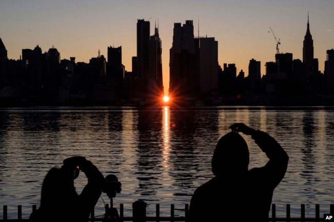 FILE - People view a Manhattanhenge sunrise along 42nd street in New York's Manhattan borough on Nov. 29, 2020, as viewed from Weehawken, N.J. There's still time to catch Manhattanhenge, when the setting sun aligns with the Manhattan street grid and bathes the urban canyons in a rosy glow. The last two Manhattanhenge sunsets of 2022 are Monday and Tuesday, July 11-12. (AP Photo/Yuki Iwamura, File)