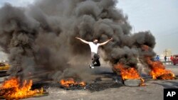 Seorang demonstran anti-pemerintah melompati ban yang terbakar yang digunakan untuk memblokir jalan raya di Baghdad, Irak, 19 Januari 2020. (Foto: AP)