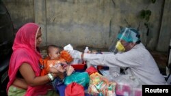 Un médico consulta a un infante junto a su madre en una clínica móvil instaurada en Ahmedabad, India, el 15 de junio de 2020.