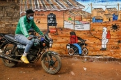 FILE - A man rides a motorcycle past an informational mural warning people about the dangers of the new coronavirus, in the Kibera slum, or informal settlement, of Nairobi, Kenya, July 8, 2020.