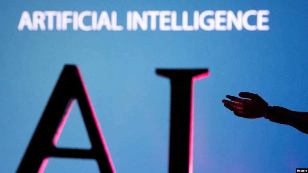 Las iniciales en glés de Inteligencia Artificial, pueden observarse en una pantalla gigante junto a una miniatura de mano de robot en esta ilustración tomada el 23 de junio de 2023.