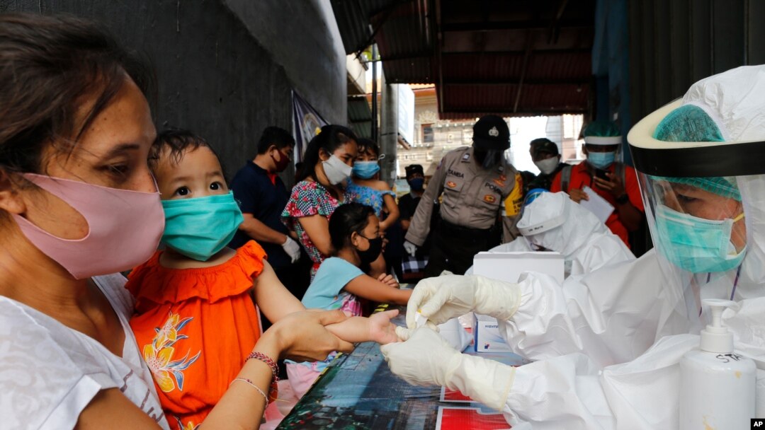 A mother holds her daughter to receive a coronavirus antibody test from health workers at a village in Bali, Indonesia, May 27, 2020. 