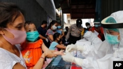 A mother holds her daughter to receive a coronavirus antibody test from health workers at a village in Bali, Indonesia, May 27, 2020. 