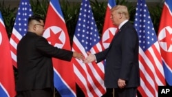 Le président américain Donald Trump tend la main au dirigeant nord-coréen Kim Jong Un à la station balnéaire de Capella sur l'île de Sentosa le mardi 12 juin 2018 à Singapour.