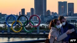 Dua orang yang mengenakan masker mengambil swafoto di depan Olympic Rings, di taman Odaiba Seaside, Tokyo yang akan menjadi lokasi Olimpiade 2020 (foto: dok).