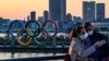 Dua pengunjung yang mengenakan masker berpose di dekat logo "Cincin Olimpiade" di Odaiba Seaside Park, Tokyo (foto: ilustrasi). Pelaksanaan olimpiade terancam oleh wabah virus corona. 