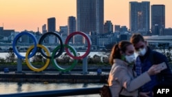 Dua pengunjung yang mengenakan masker berpose di dekat logo "Cincin Olimpiade" di Odaiba Seaside Park, Tokyo (foto: ilustrasi). Pelaksanaan olimpiade terancam oleh wabah virus corona. 