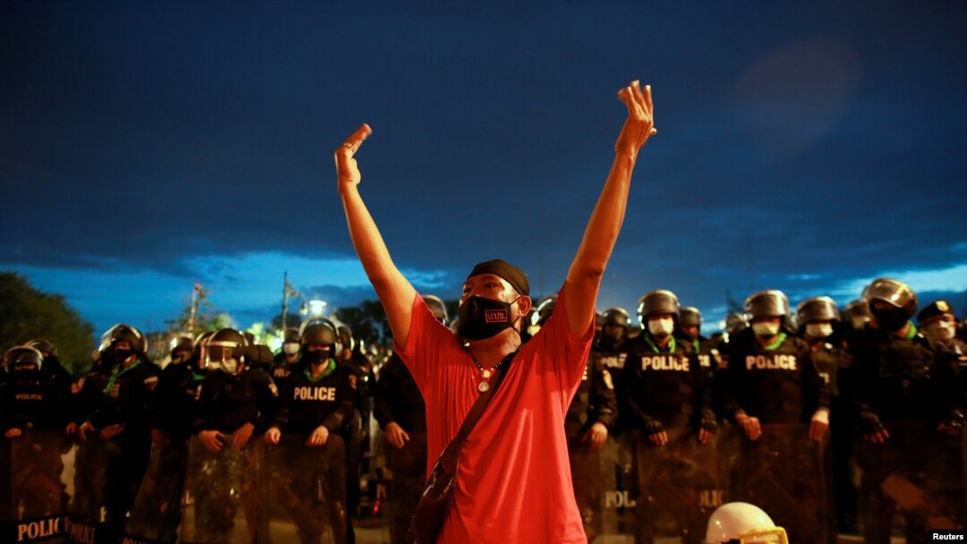 A protester gestures as police stand guard near the Government House during a demonstration marking the 89th anniversary of the abolition of absolute monarchy, in Bangkok, Thailand, June 24, 2021. 