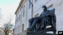 La estatua de John Harvard, en la prestigiosa universidad que lleva su nombre, fue decorada con una mascarilla en los días más críticos de la pandemia. Ahora la universidad se prepara para recibir a una parte de sus estudiantes.